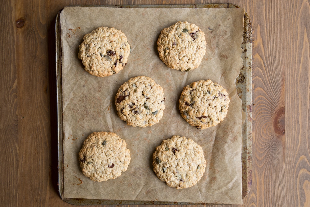 Freshly baked vegan oat cookies on a baking tray lined with baking paper.