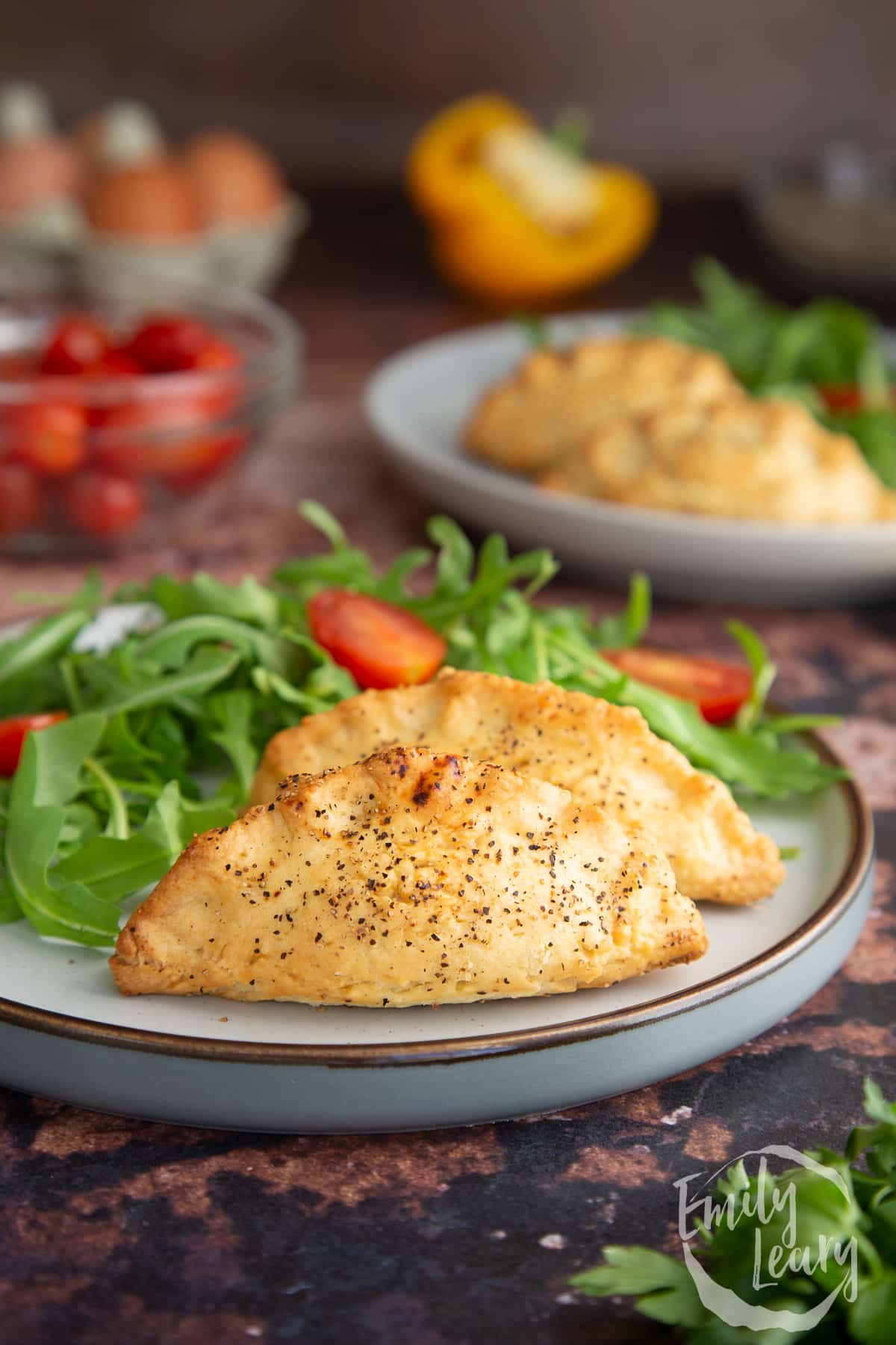 Side on shot of two finished mini cornish pasties on a decorative plate served with a side salad.