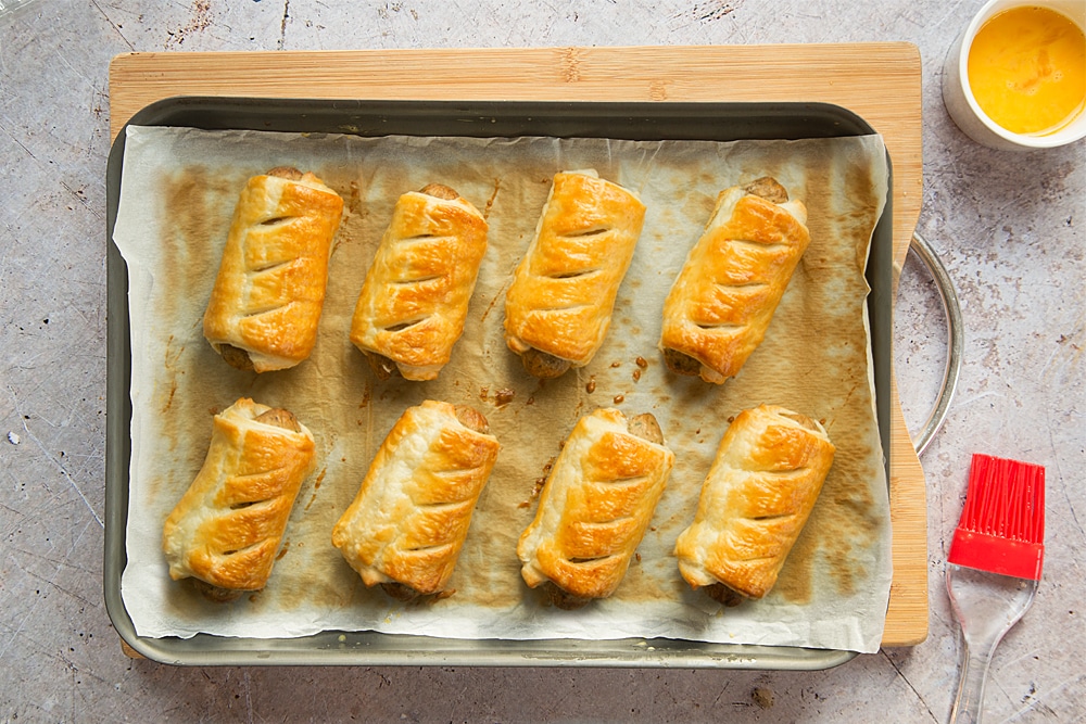 Eight cooked vegetarian sausage rolls on a baking tray lined with baking paper.