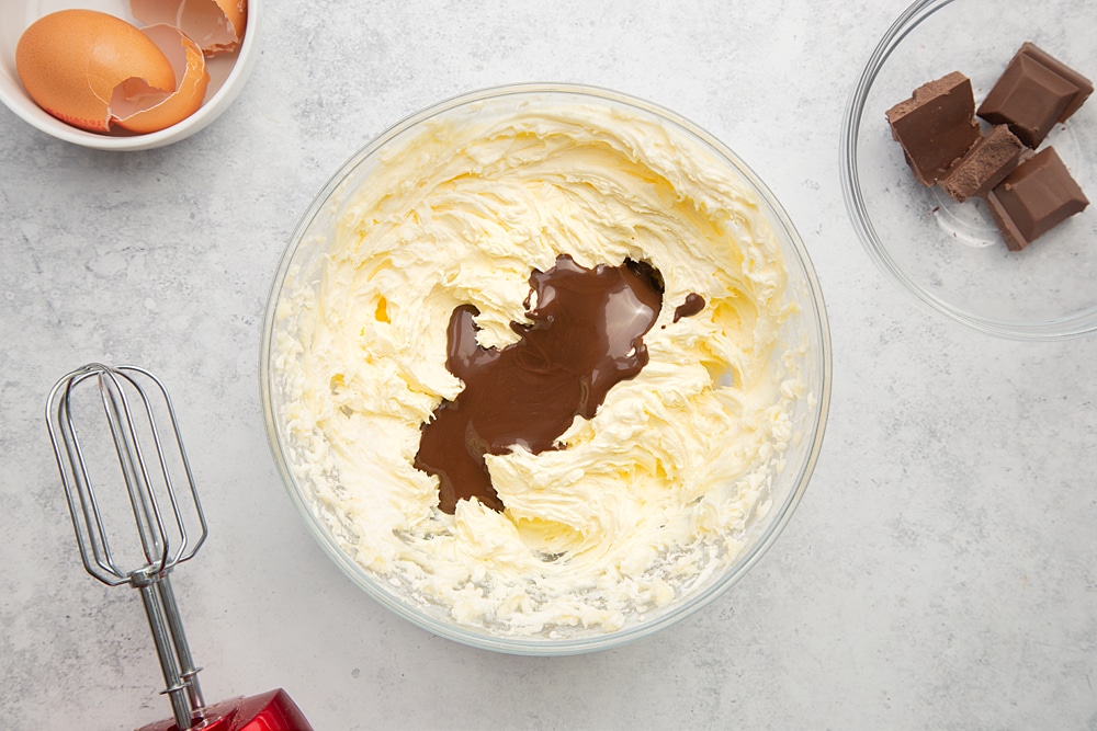 Adding the melted chocolate to the bowl of ingredients for the frosting which will be used to create the chocolate chip mini-loaf cake with chocolate frosting.