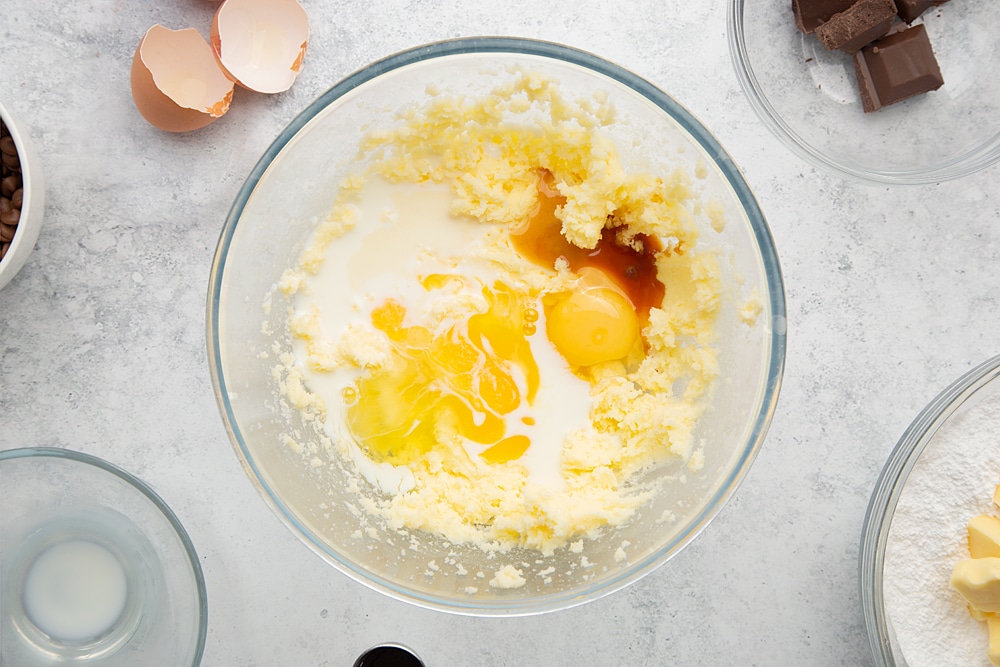 Adding eggs and flavouring to the pyrex bowl filled with ingredients required to make the chocolate chip mini-loaf cake with chocolate frosting.