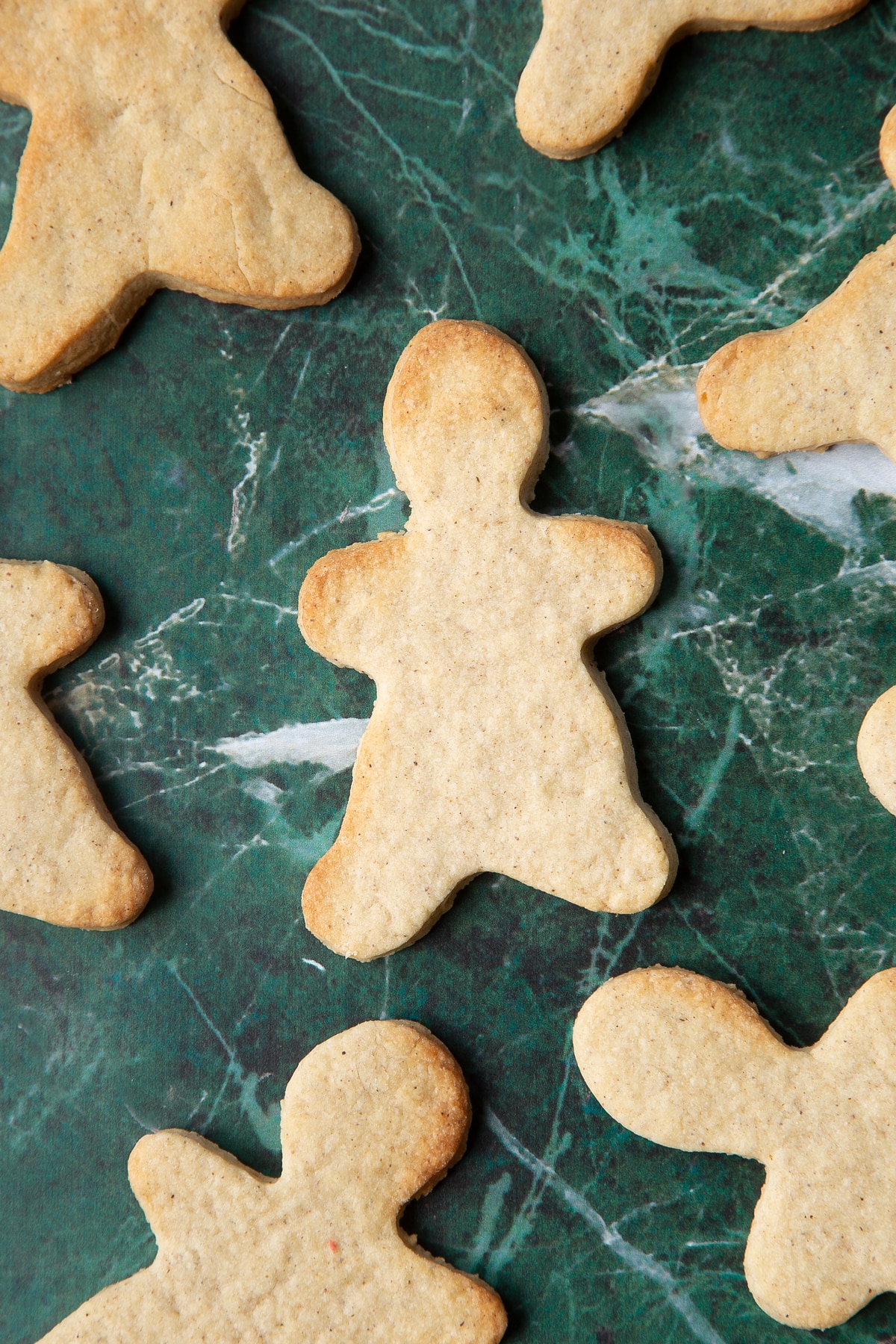 Cookies in the shape of gingerbread men on a green marble surface.