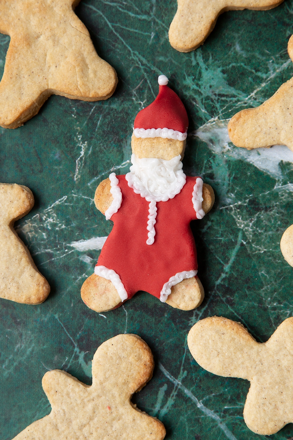 A cookie in the shape of a man, decorated with a suit and hat made from red sugar paste and white writing icing.