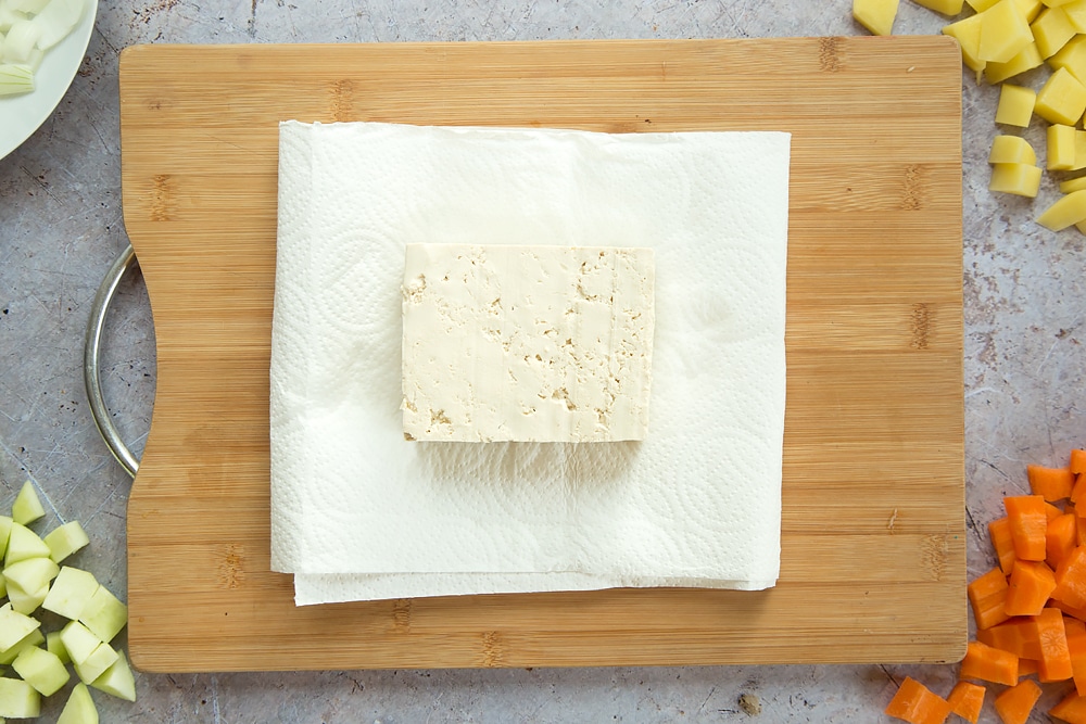 Overhead shot of tofu placed on some kitchen towel on a wooden board
