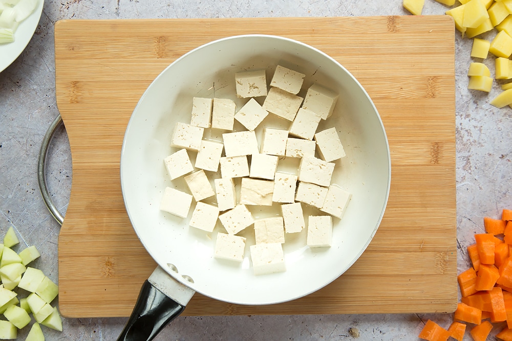 Overhead shot of sliced tofu in a large pan on a wooden board