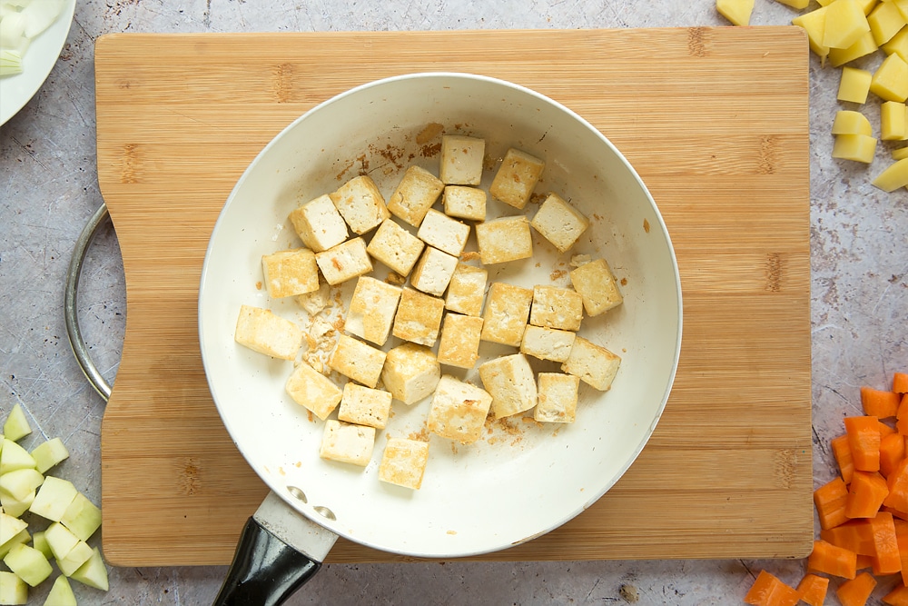 Overhead shot of fried tofu in a large white pan on a wooden board