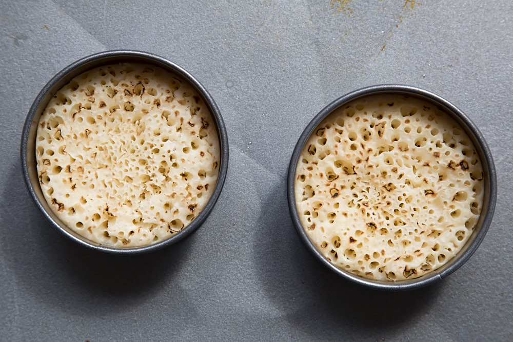 Overhead shot of two egg rings with crumpets inside.
