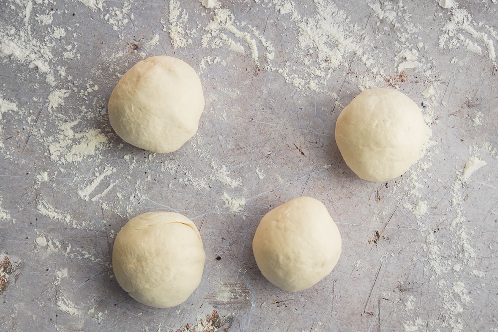 a smooth dough ball cut into four smaller dough balls on a floured surface.