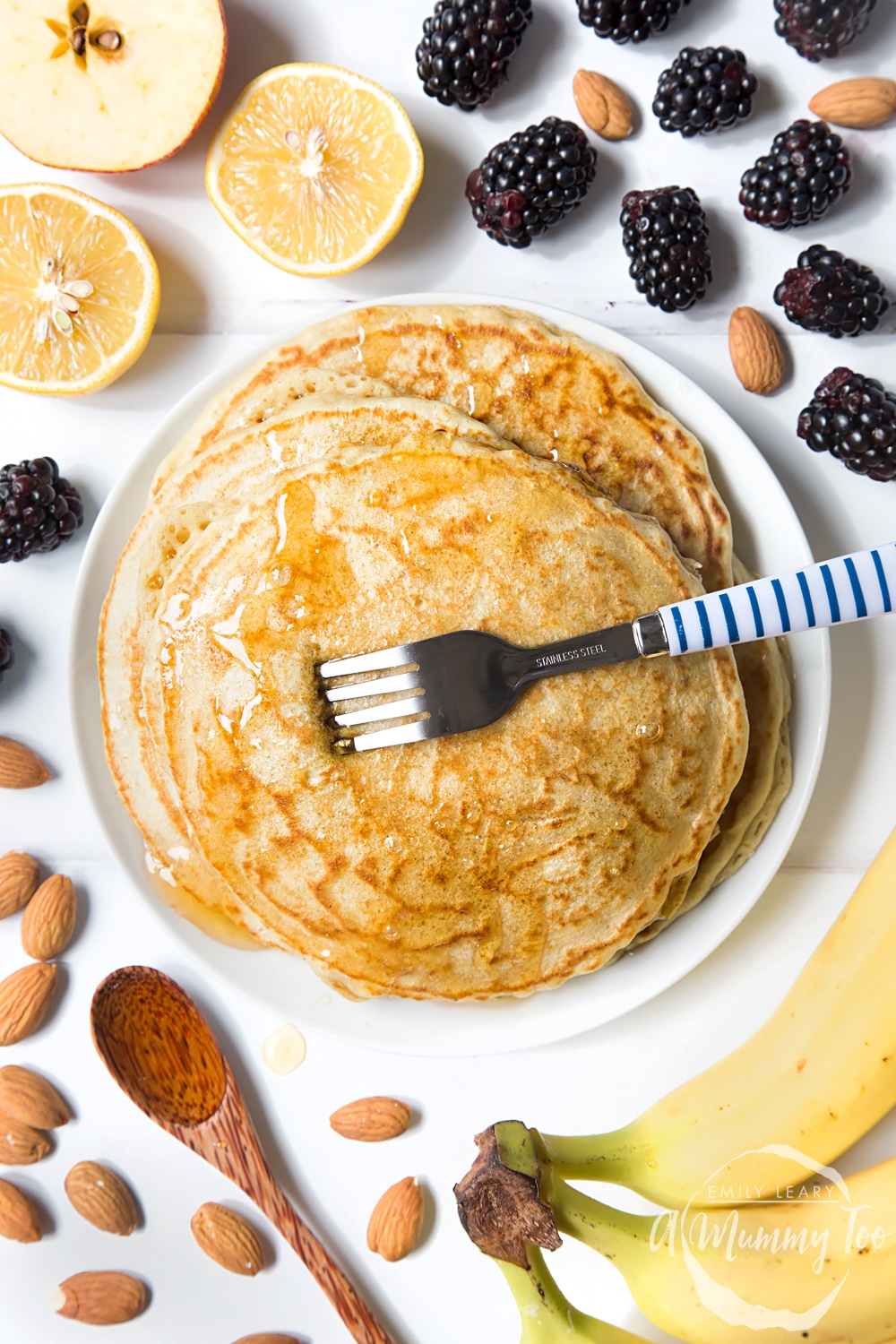 A stack of Vegan american pancakes topped with syrup, surrounded by berries and nuts