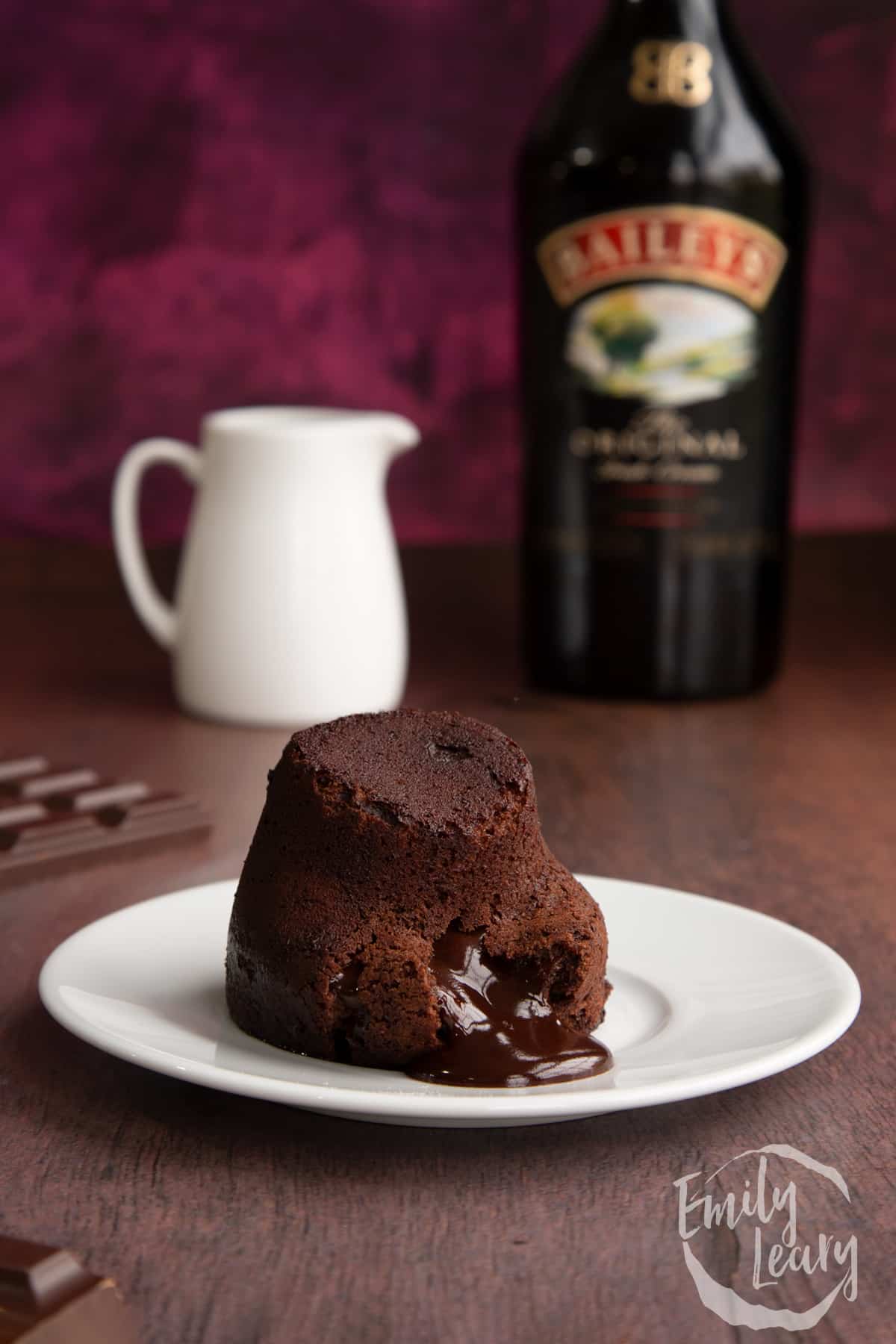Baileys lava cake on a white plate with a bottle of baileys in the background.