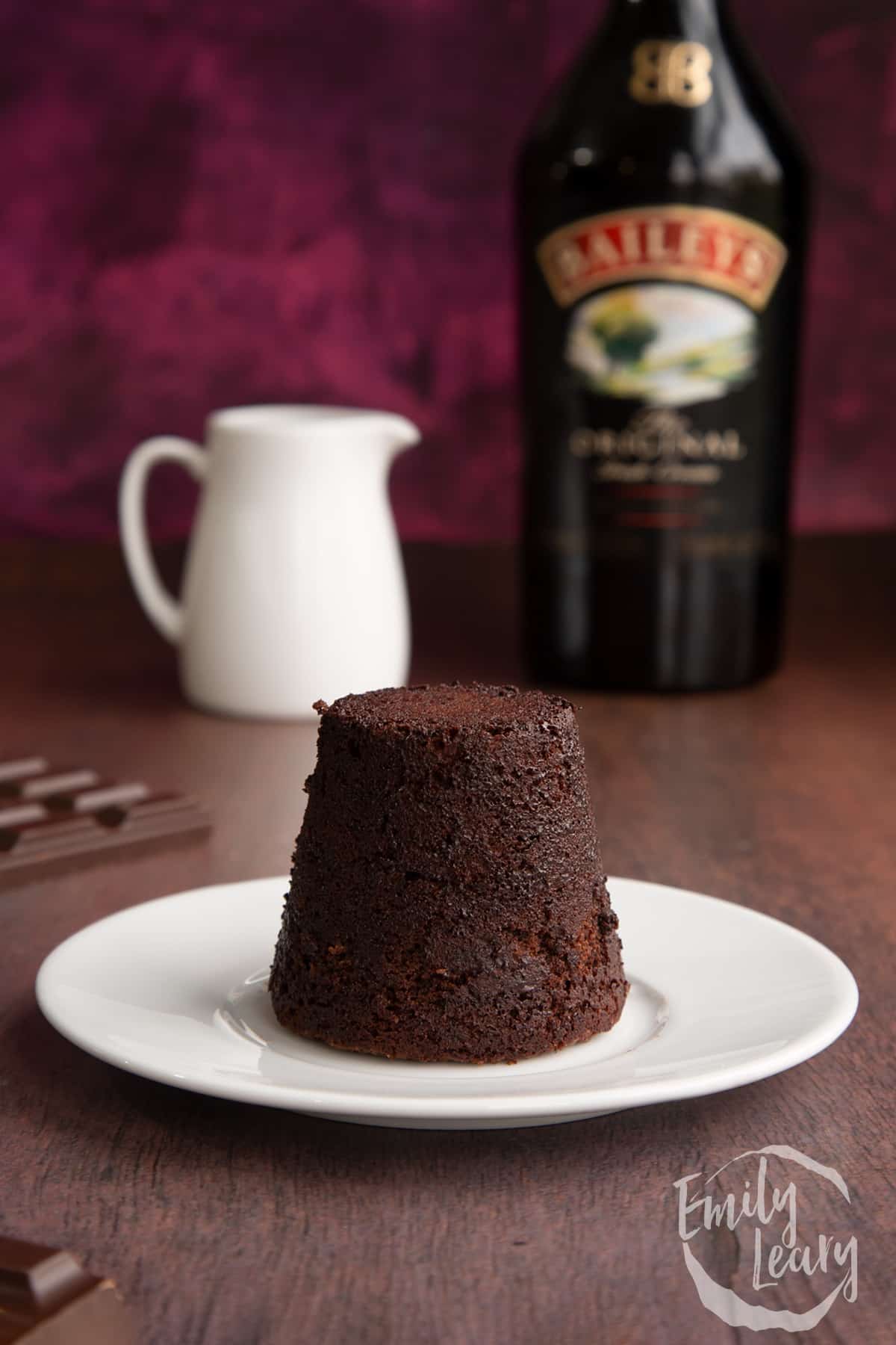 Baileys lava cake on a white plate with a bottle of baileys in the background cut open by a spoon.