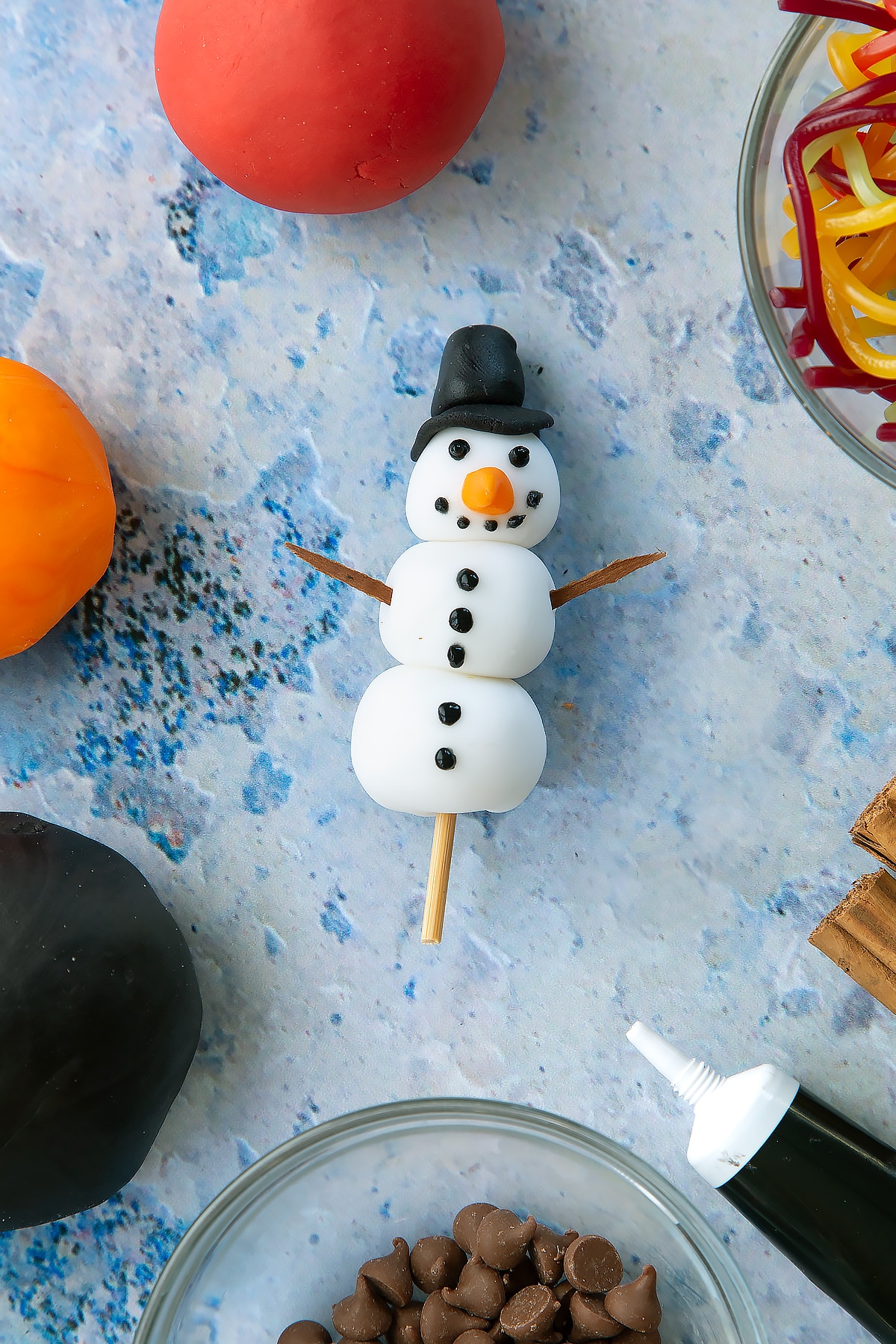 Overhead shot of the finished sugar paste snowman complete with cinnamon park as arms and icing for added details such as the eyes and buttons.