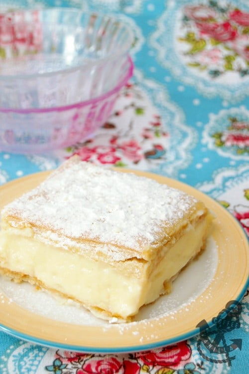a piece of Polish Custard Cream Pie on a yellow and blue plate topped with icing sugar.