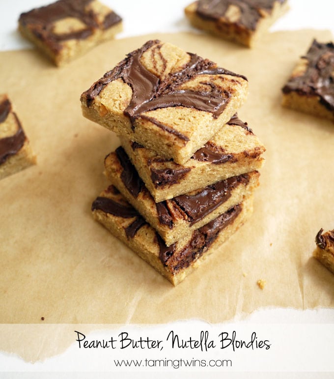a stack of Peanut Butter Nutella Blondies on a piece of greaseproof paper with more Peanut Butter Nutella Blondies in the background.