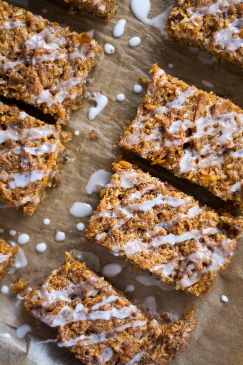 close up of Vegan Carrot Cake Bars drizzled with icing on a greaseproof paper backing.