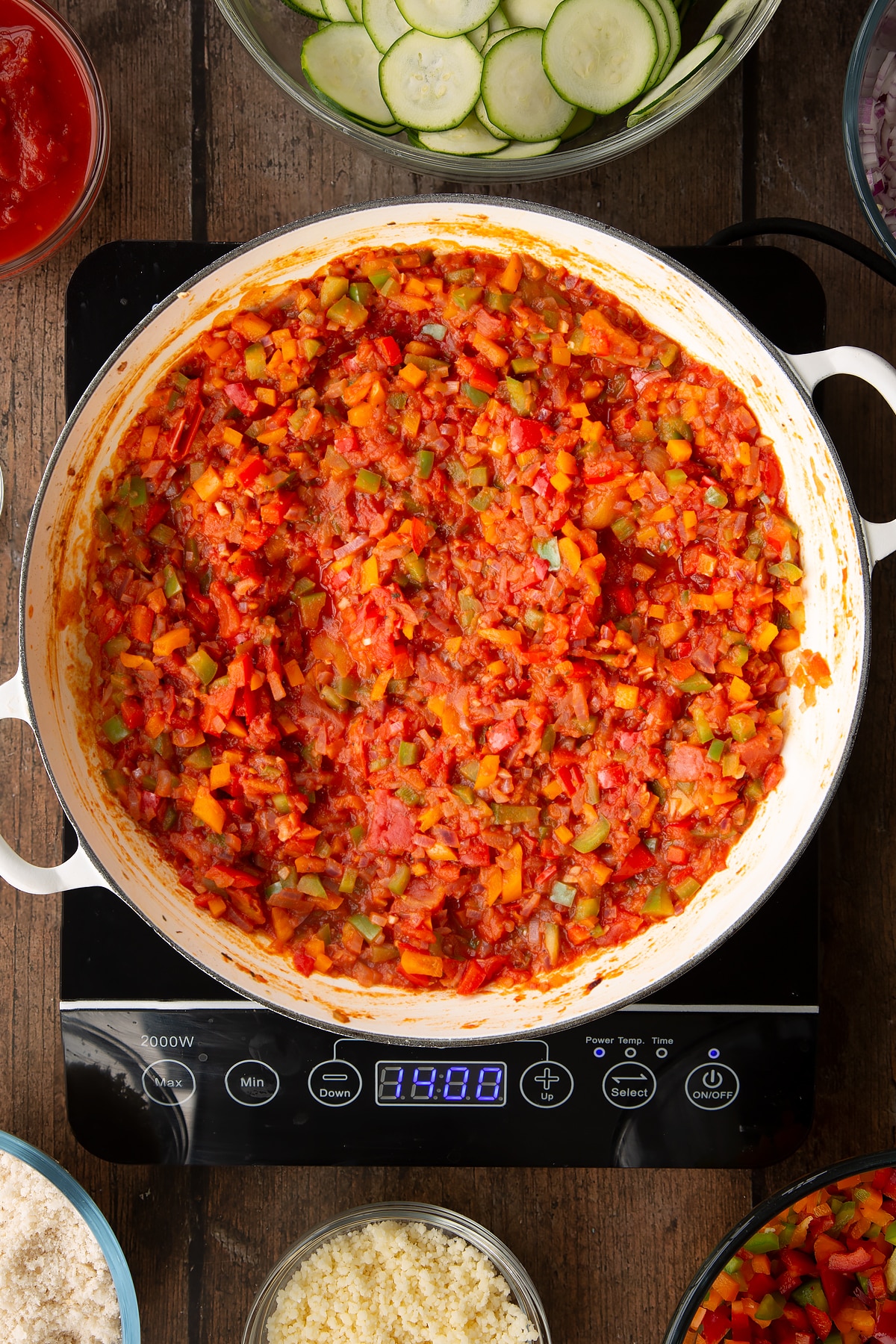 tomato and courgette gratin base in a large white frying pan on an induction hob.