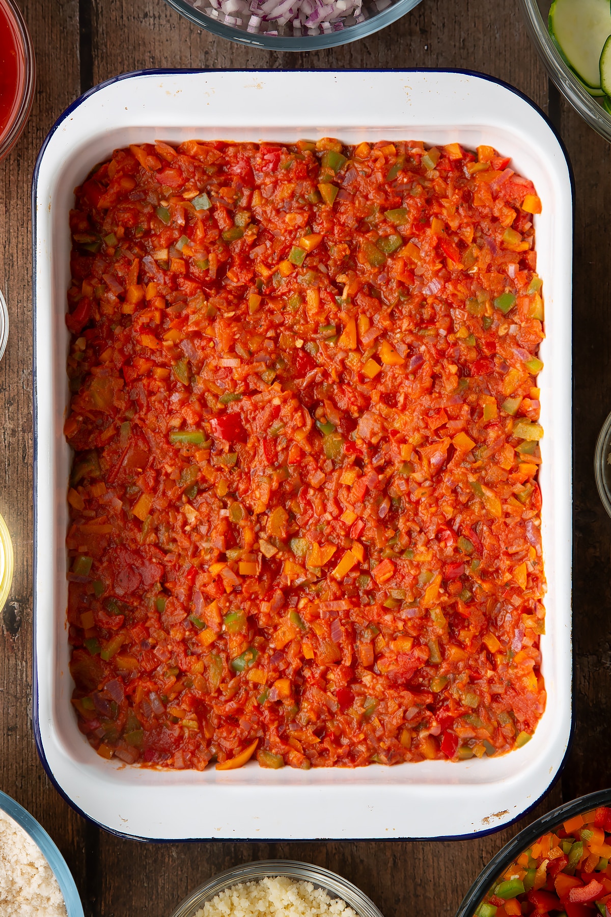 tomato, pepper and onion sauce in the bottom of a white roasting dish.