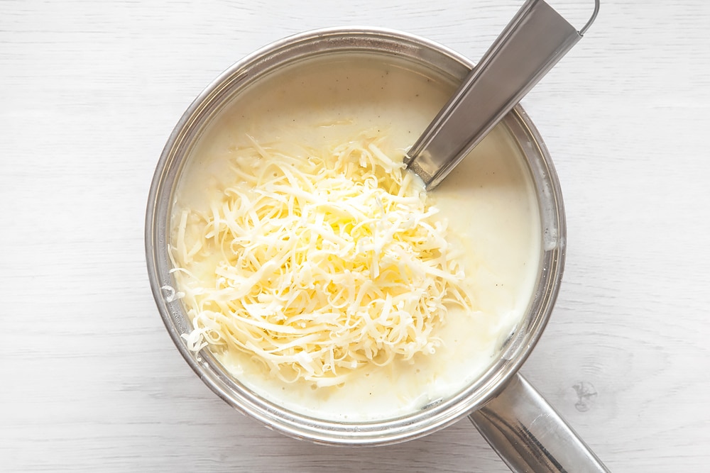 Adding cheese to the white sauce for your mini cheesy fish pies