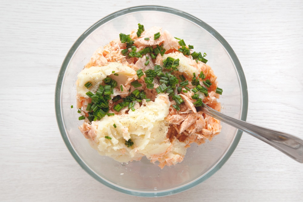 Adding ingredients including the flaked salmon, potato and finely chopped chives into a mixing bowl.