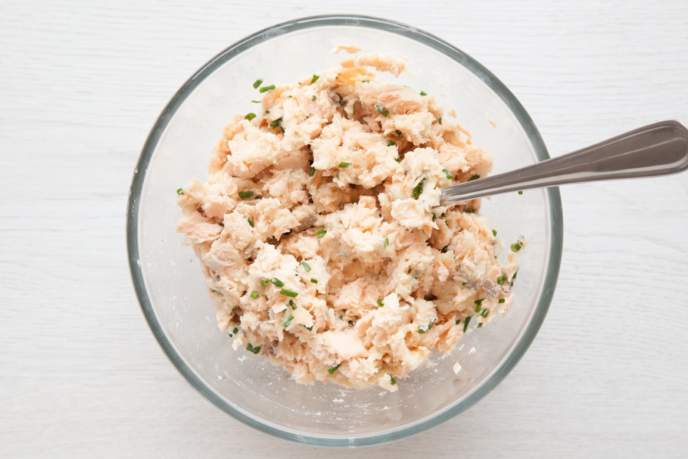 Salmon fishcake mix in a bowl with a fork on the side. The bowl is set on a light wooden background.