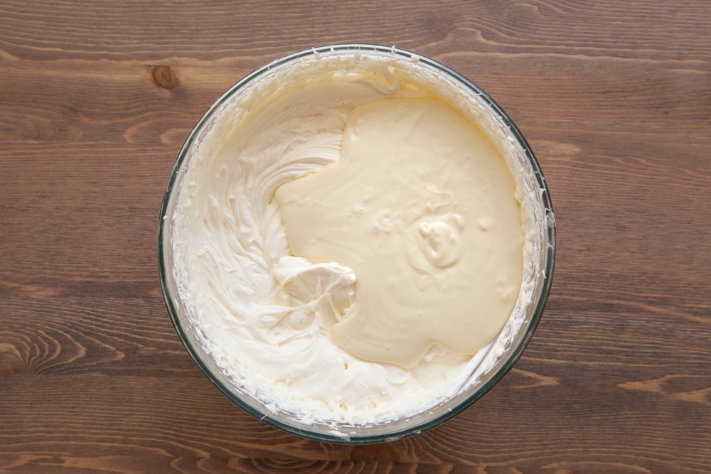 A bowl containing cream cheese, double cream, vanilla and sugar beaten together, topped with melted white chocolate.