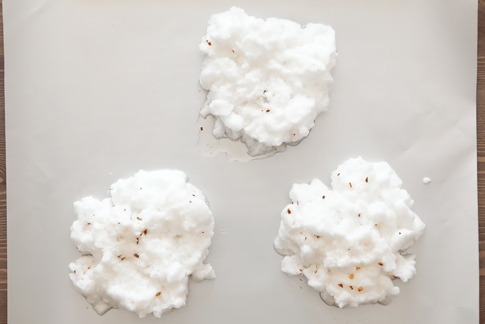 The whites for spicy eggs in clouds spread in three piles on a baking tray.