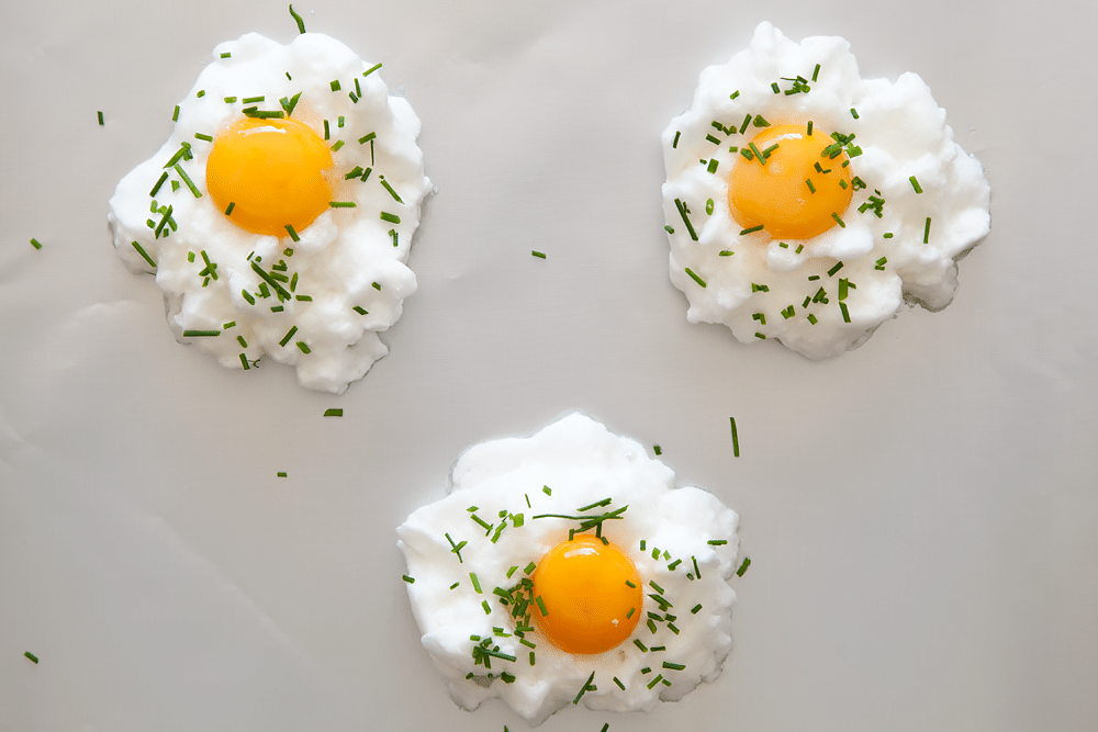 Eggs in clouds sprinkled with chives on a baking tray - ready to bake.