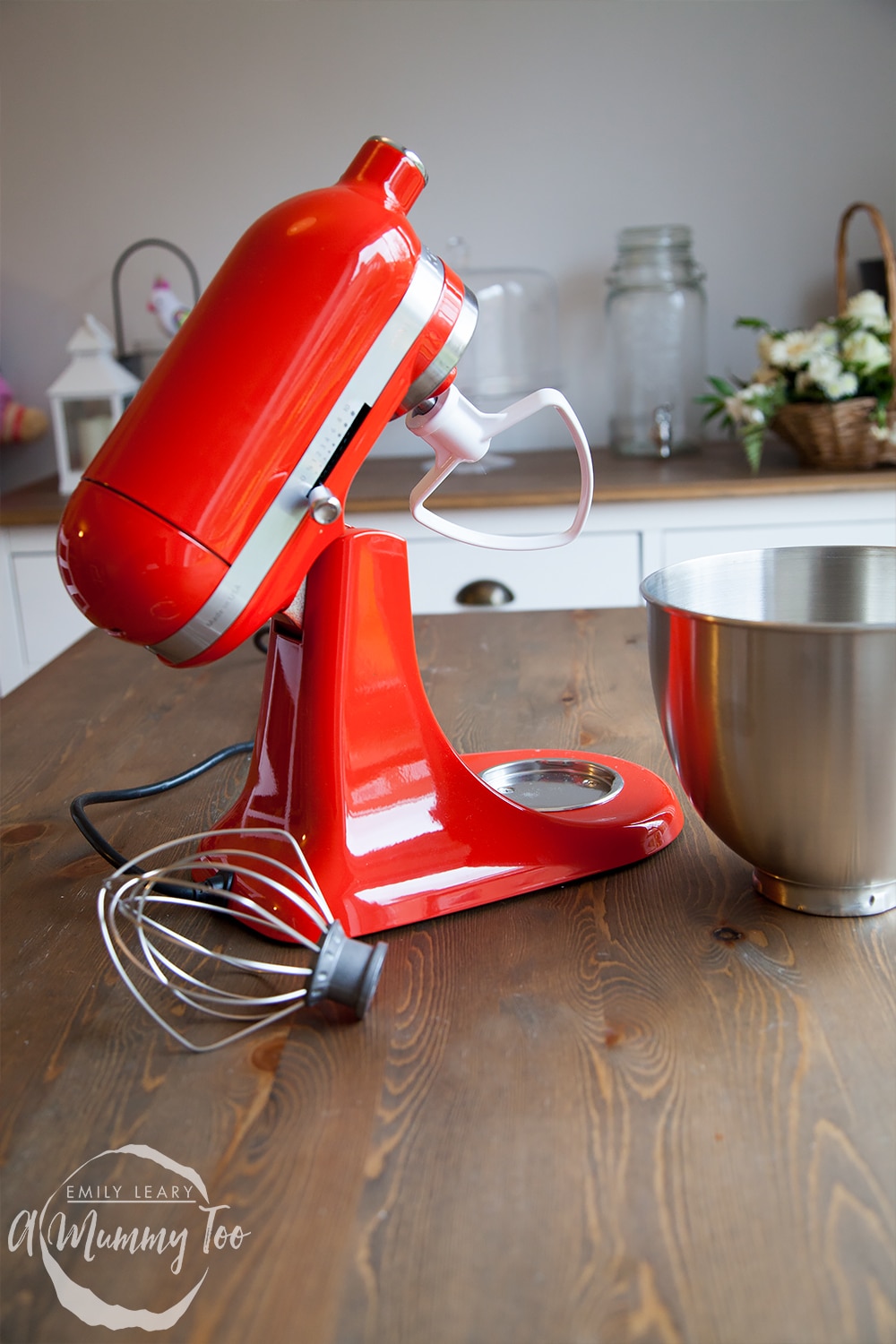 Red KitchenAid mini on a wooden counter surface surrodunded by the accessories included with the appliance.
