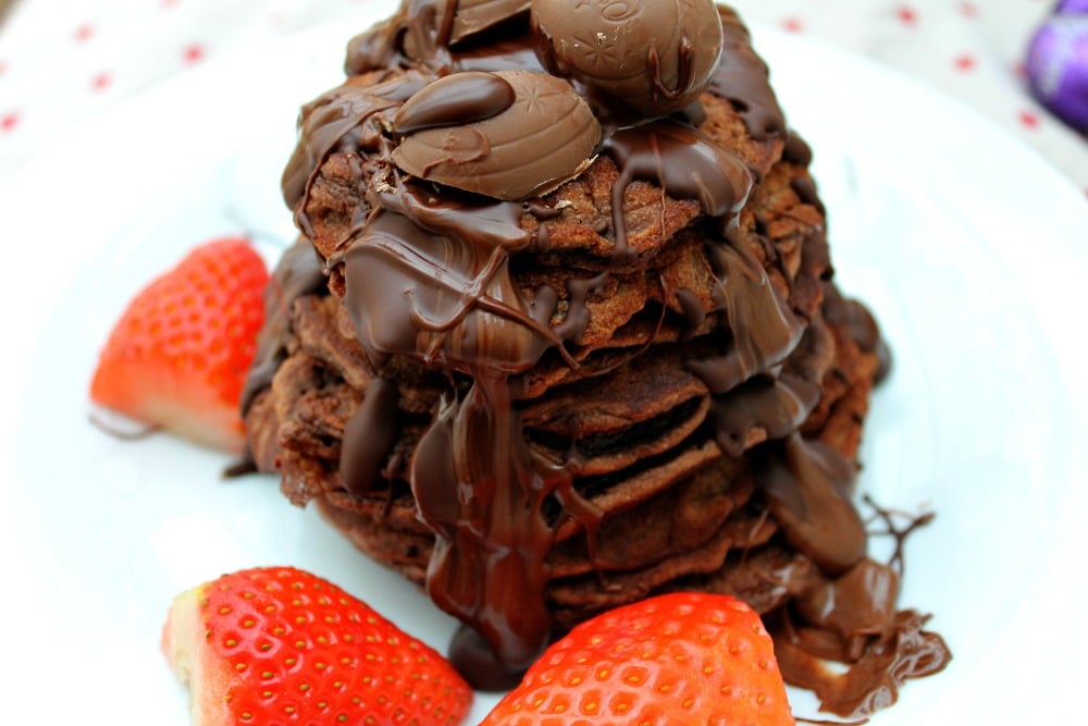 nutella spelt pancakes by baking queen 74 stacked on a white plate surrounded by berries and topped with chocolate sauce