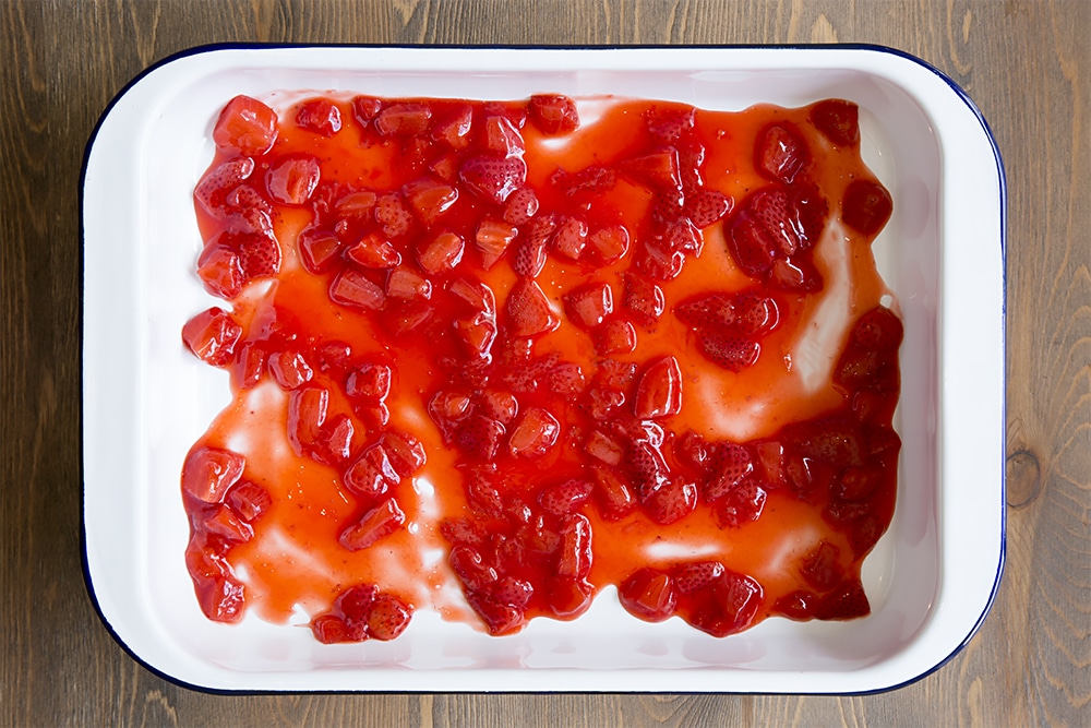 Strawberry jelly mixture poured into a white metal dish on a wooden background.