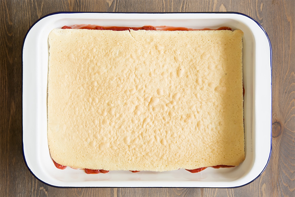 white metal dish with a strawberry mixture topped with a thin layer of vanilla sponge.