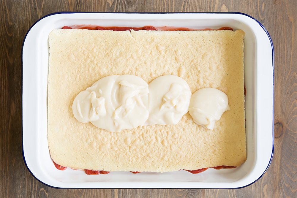 white metal dish with a strawberry mixture topped with a thin layer of vanilla sponge and white egg mixture.