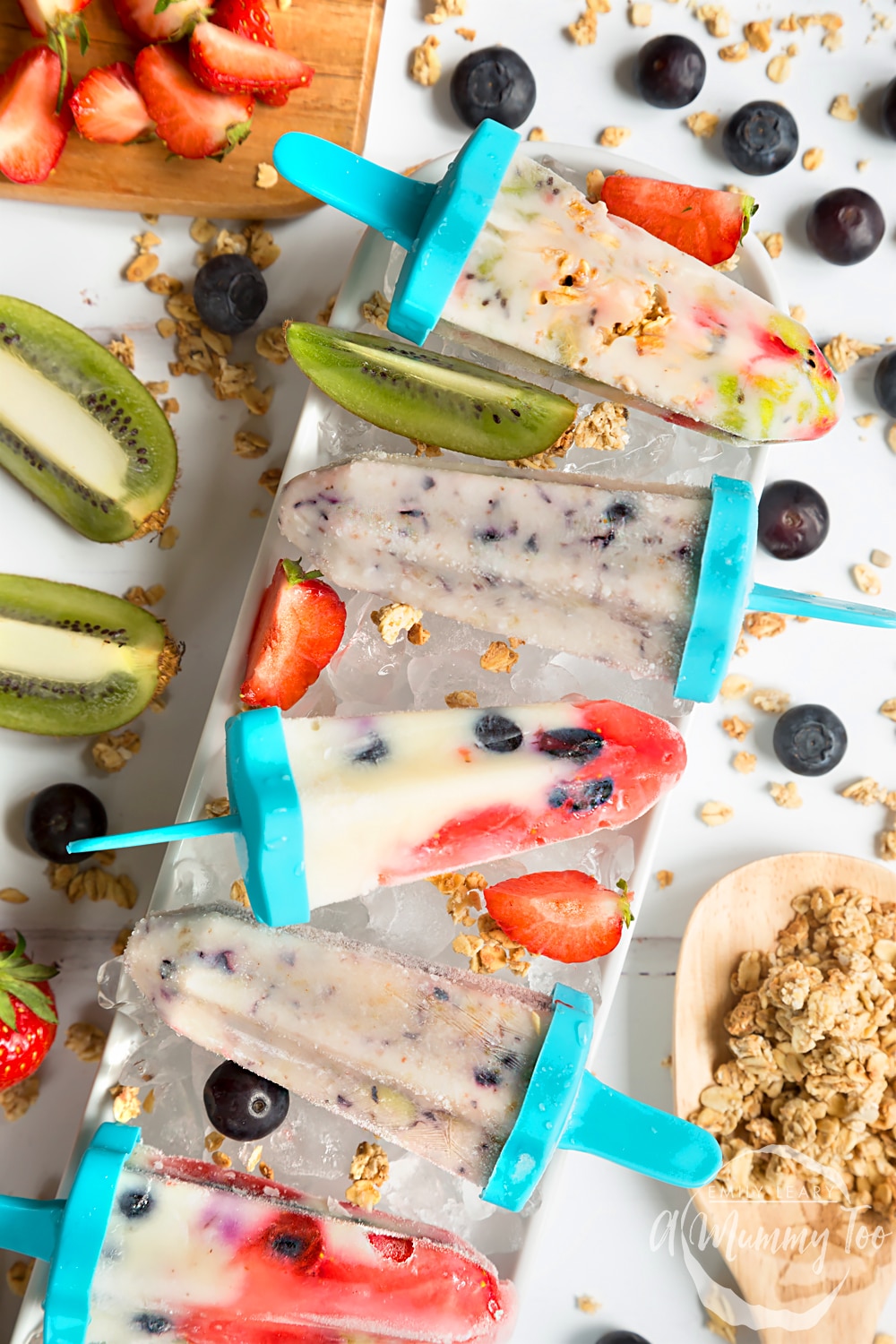 Frozen fruit and yogurt lollies shown surrounded by kiwis, strawberries, blueberries and granola. Perfect for a refreshing treat this Summer!