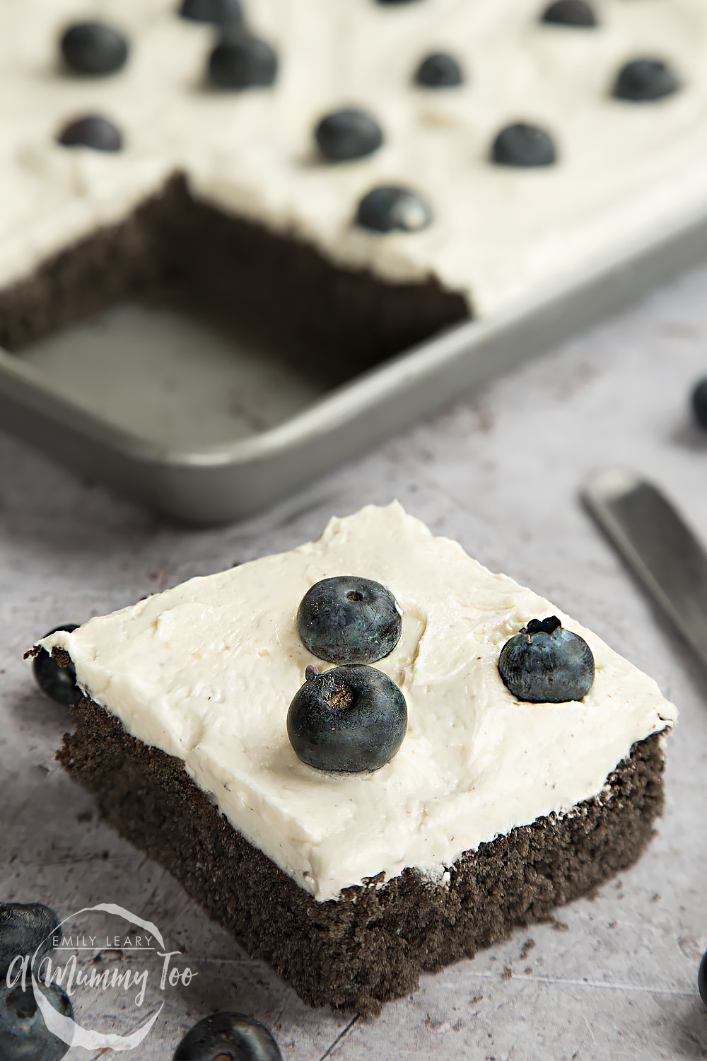 A slice of black velvet sheet cake with classic velvet frosting, topped with blueberries