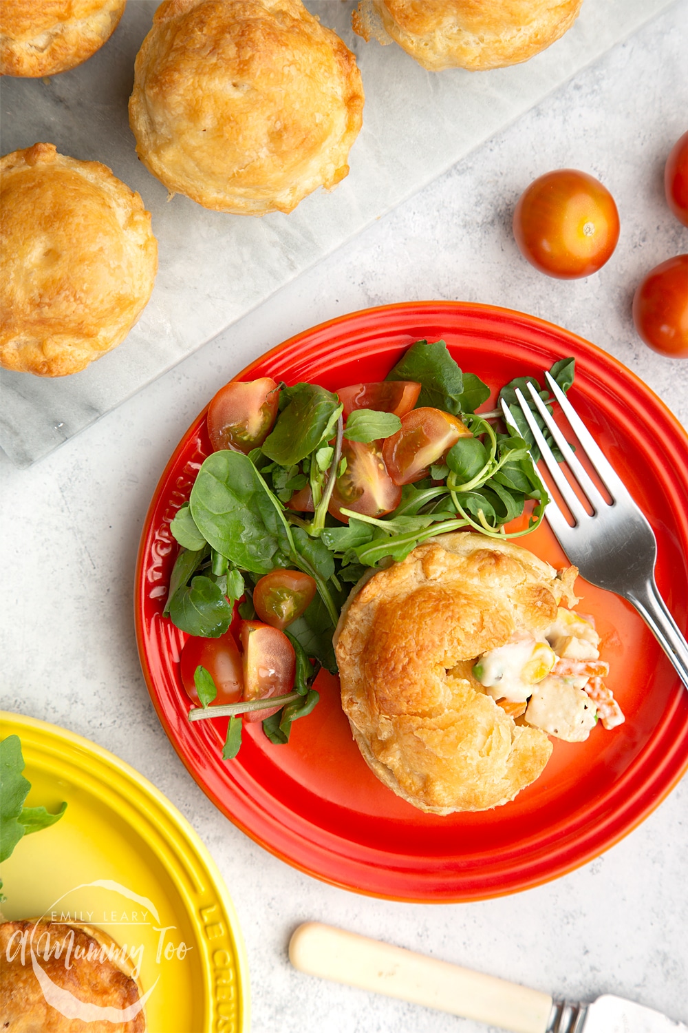 A cut open vegan pie on a red plate with a side salad. At the side there's a yellow plate with the same dish and some additional pies on a marble chopping board.