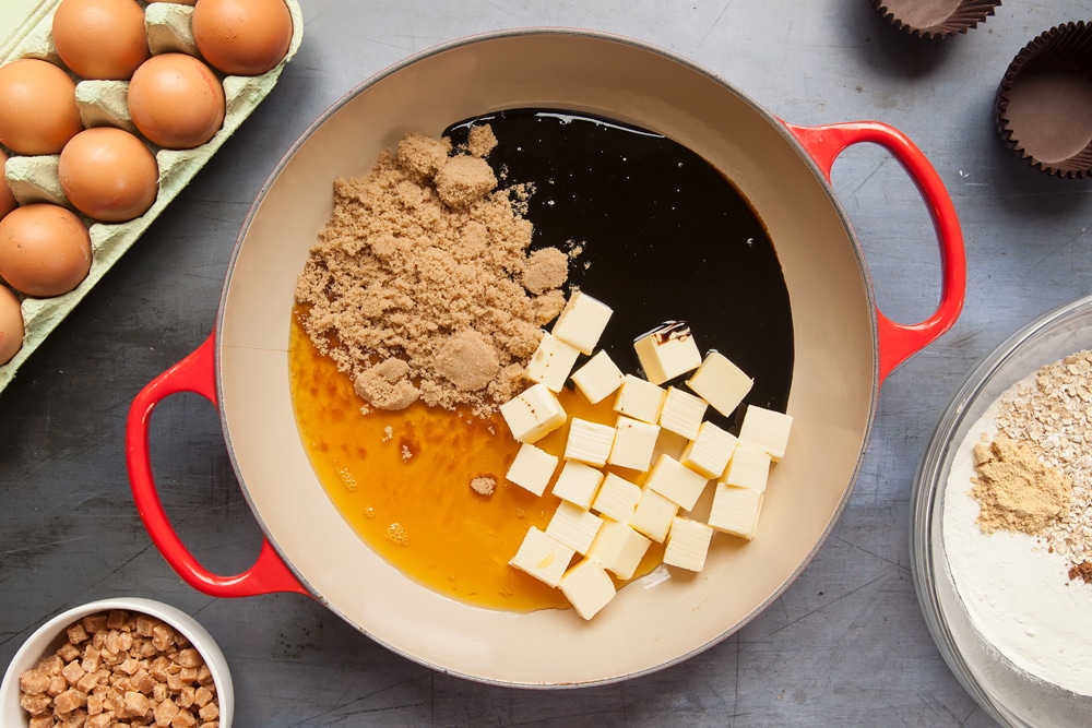 Overhead shot of butter, sugar, eggs, golden syrup, and black treacle in a red pan
