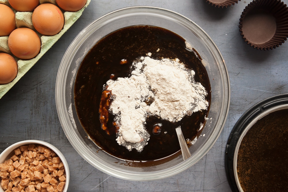 Overhead shot of dry ingredients with syrup mixture and a spoon in a large clear bowl