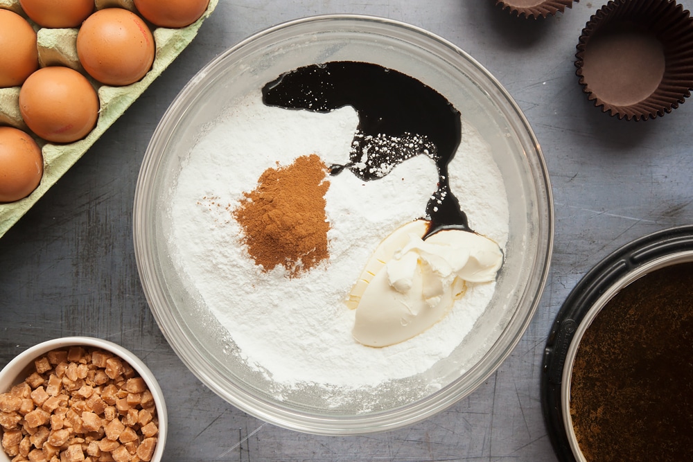 Overhead shot of frosting mix, cream cheese, cinnamon, treacle, and icing sugar in a clear bowl