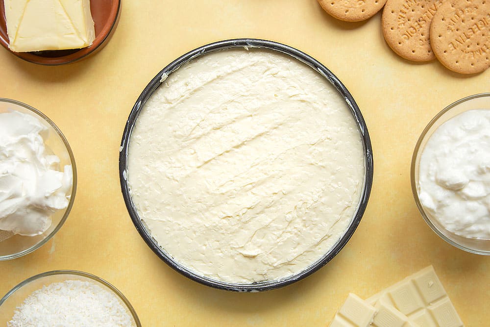 Cream cheese, yogurt, desiccated coconut and melted white chocolate spread in a cake tin with a biscuit base.