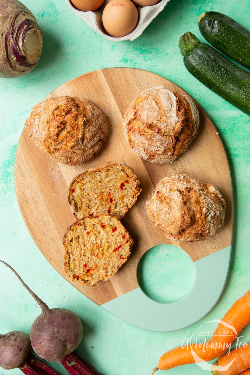 Vegetable soda bread rolls recipe - rolls arranged on a board, one cut open to show the vegetable flecked interior. Surrounded by vegetables.