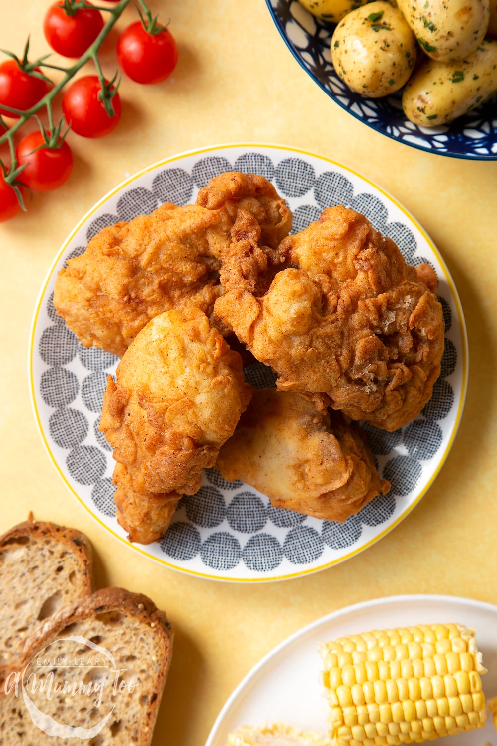 Gordon Ramsay&rsquo;s buttermilk fried chicken arranged on a plate, surrounded by tomatoes, potatoes, bread and corn on the cob.