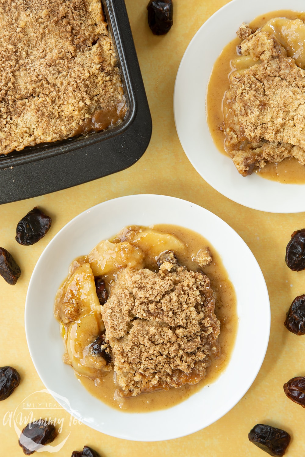 Overhead shot of two plates with toffee apple crumble. At the side there's a pan with the finished toffee apple crumble.