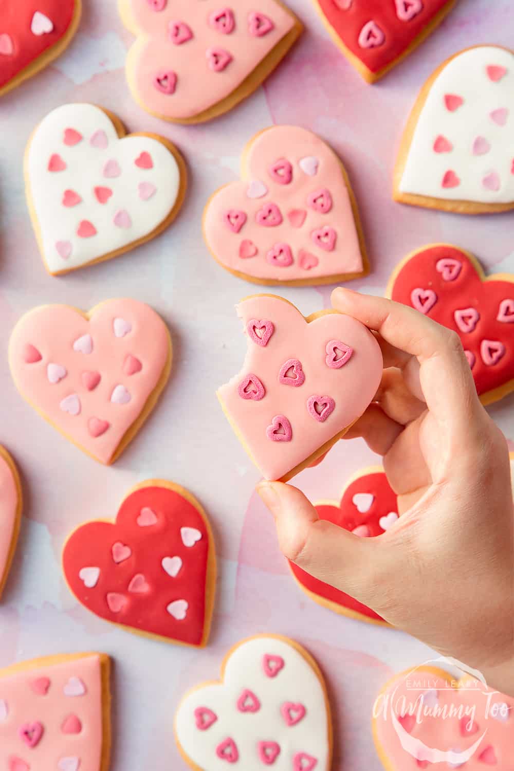 Overhead shot of a hand holding a Heart biscuit for Valentine's Day with a mummy too logo in the lower-right corner