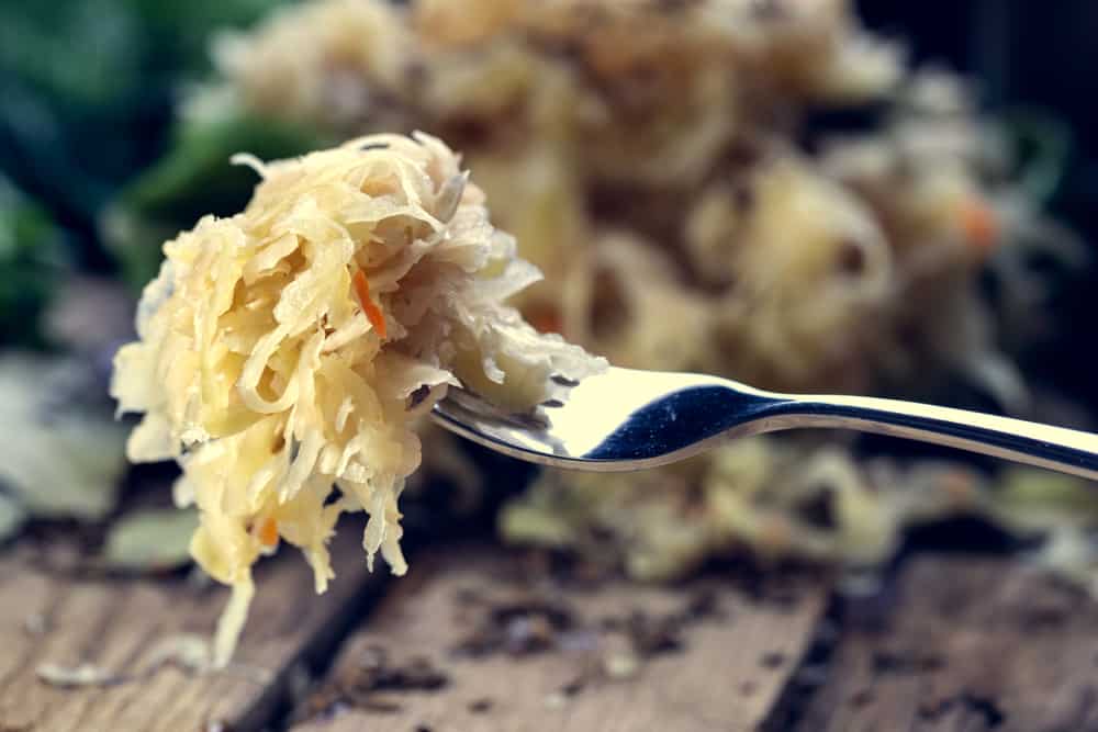 A fork filled with sauerkraut. There's a pile of sauerkraut in the background.