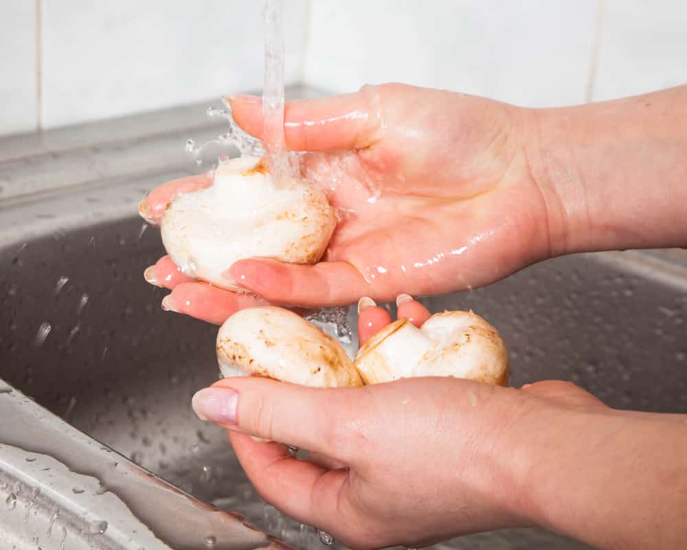 Mushrooms being rinced under running water in a metal sink.