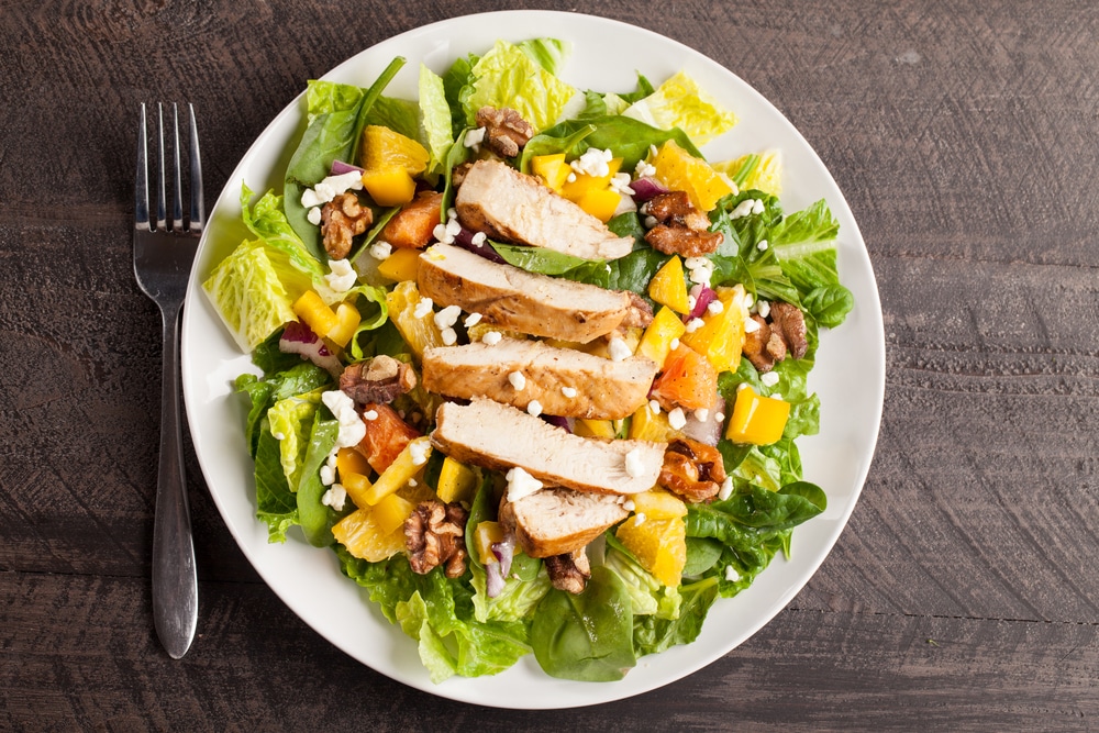 Overhead shot of sliced chikcen on a bed of salad. The salad is on a wooden table with the fork at the side.