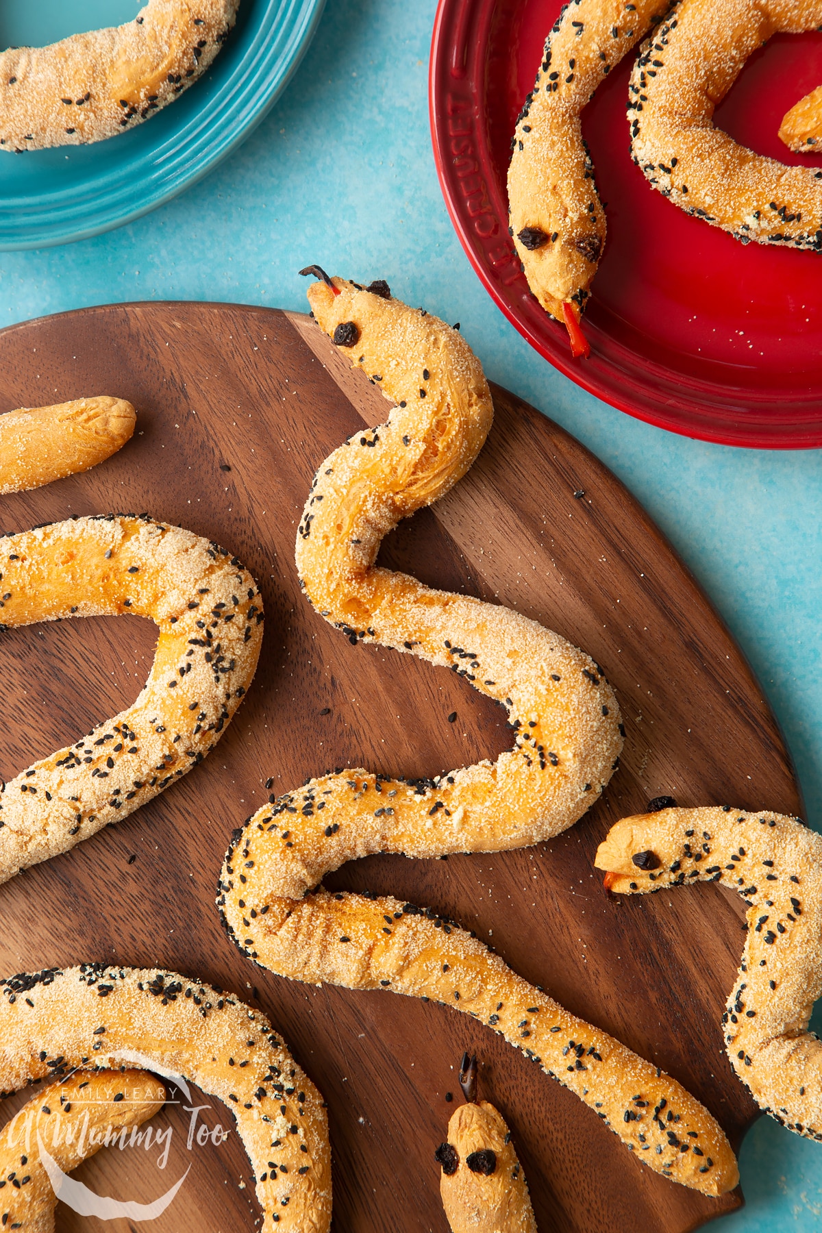 Bread snakes on a wooden board. More bread snakes are shown on coloured plates at the edges of the photo.