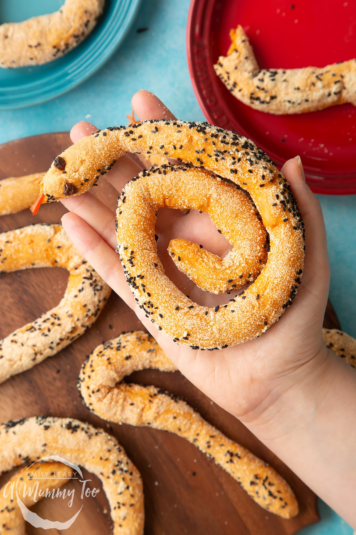 A hand holds a coiled bread snake above more on a wooden board.