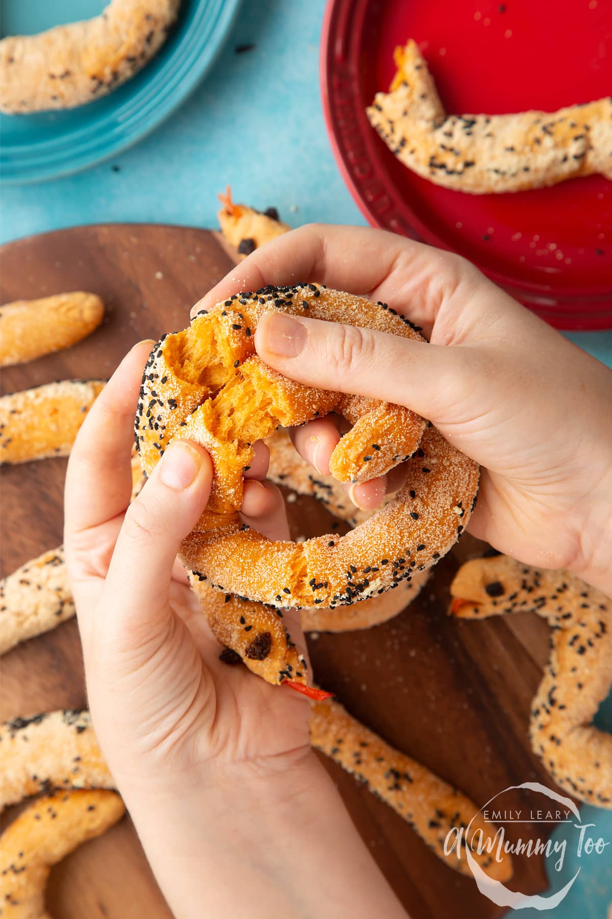 Hands holding and breaking open a bread snake above more bread snakes on a wooden board.