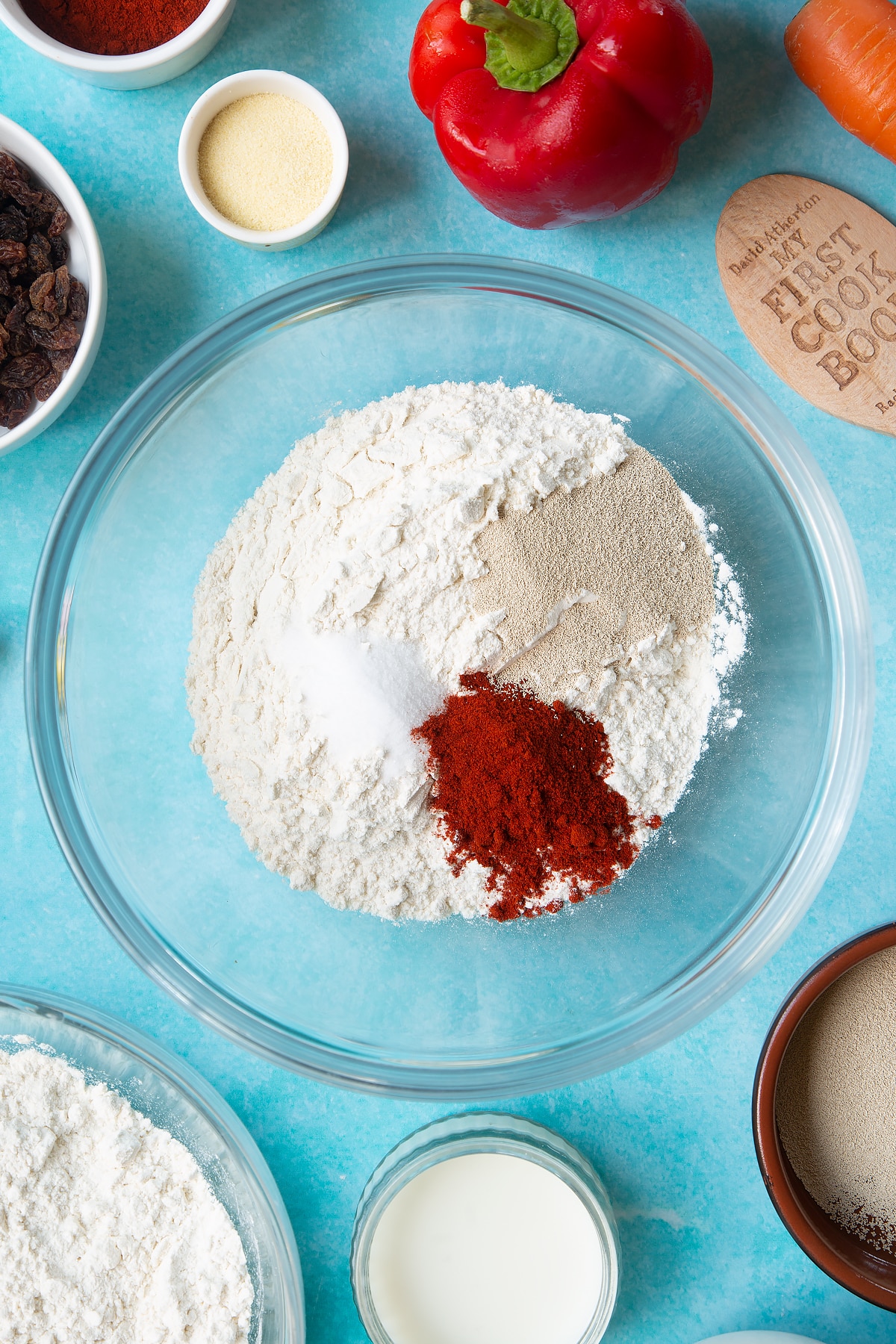 Flour, salt, paprika and yeast in a mixing bowl. Ingredients to make bread snakes surround the bowl.